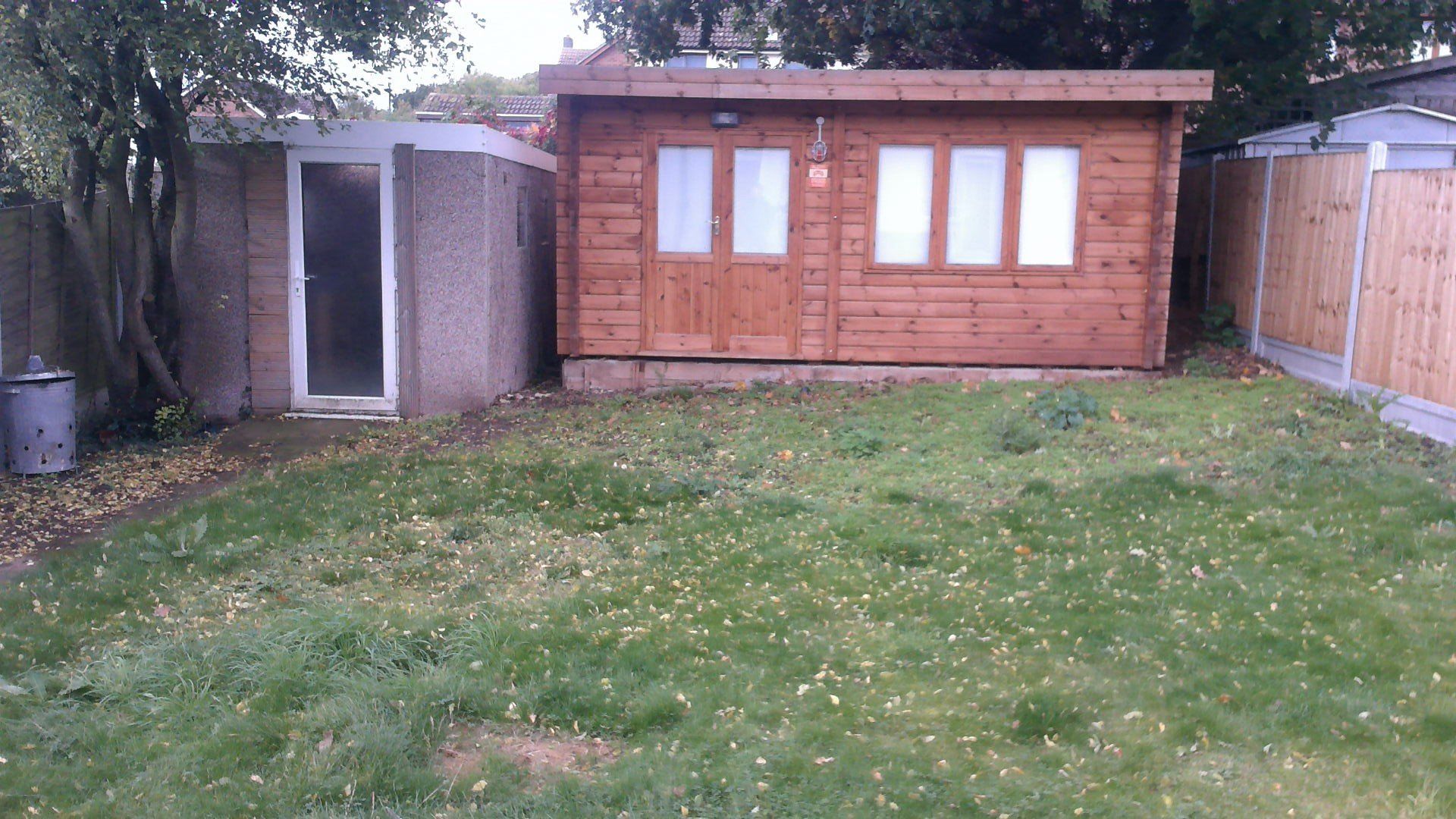 Backyard with a brown shed, a concrete structure, and patchy grass.