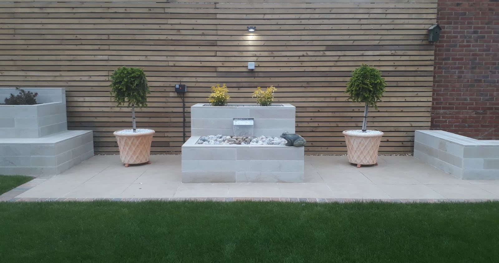Modern garden with water feature, potted trees, and horizontal wooden fence.