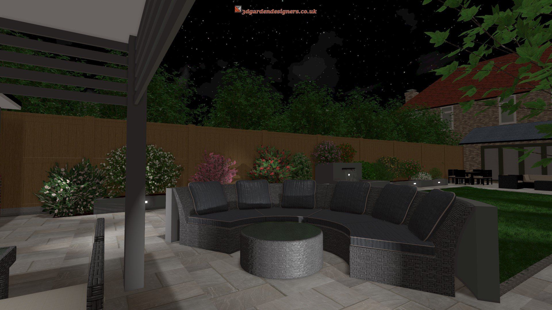 Nighttime view of a backyard patio with dark gray outdoor furniture, lush greenery, and lighting.