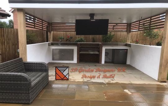 Outdoor kitchen and seating area with TV, built-in grill, and white stucco walls.