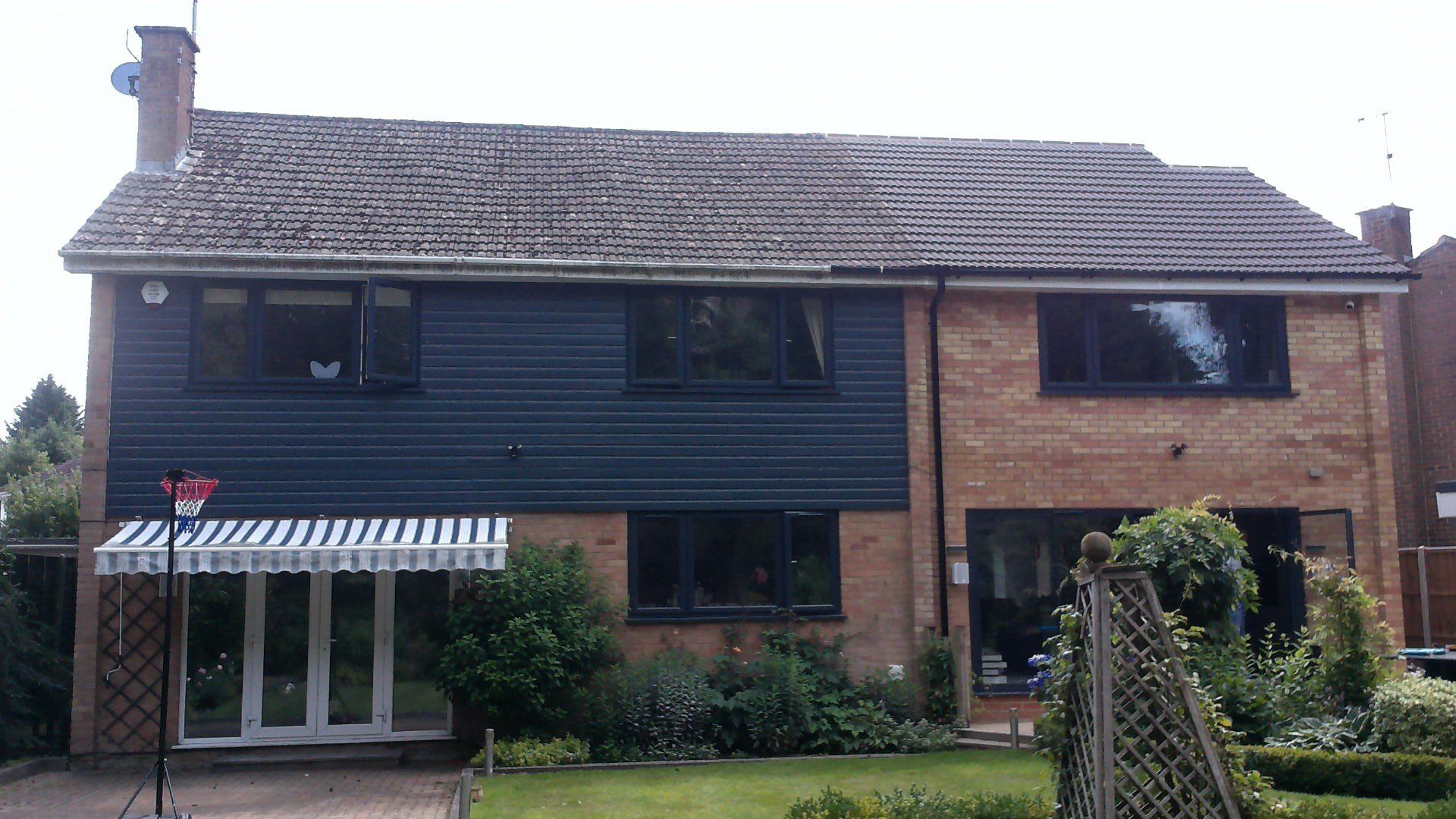 Two-story house with a blue-sided portion, brick-sided portion, and a striped awning over the glass doors.