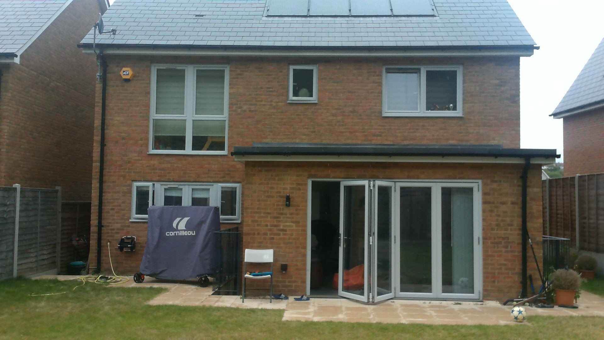 Back of a brick house with gray roof and open glass doors leading to a backyard.