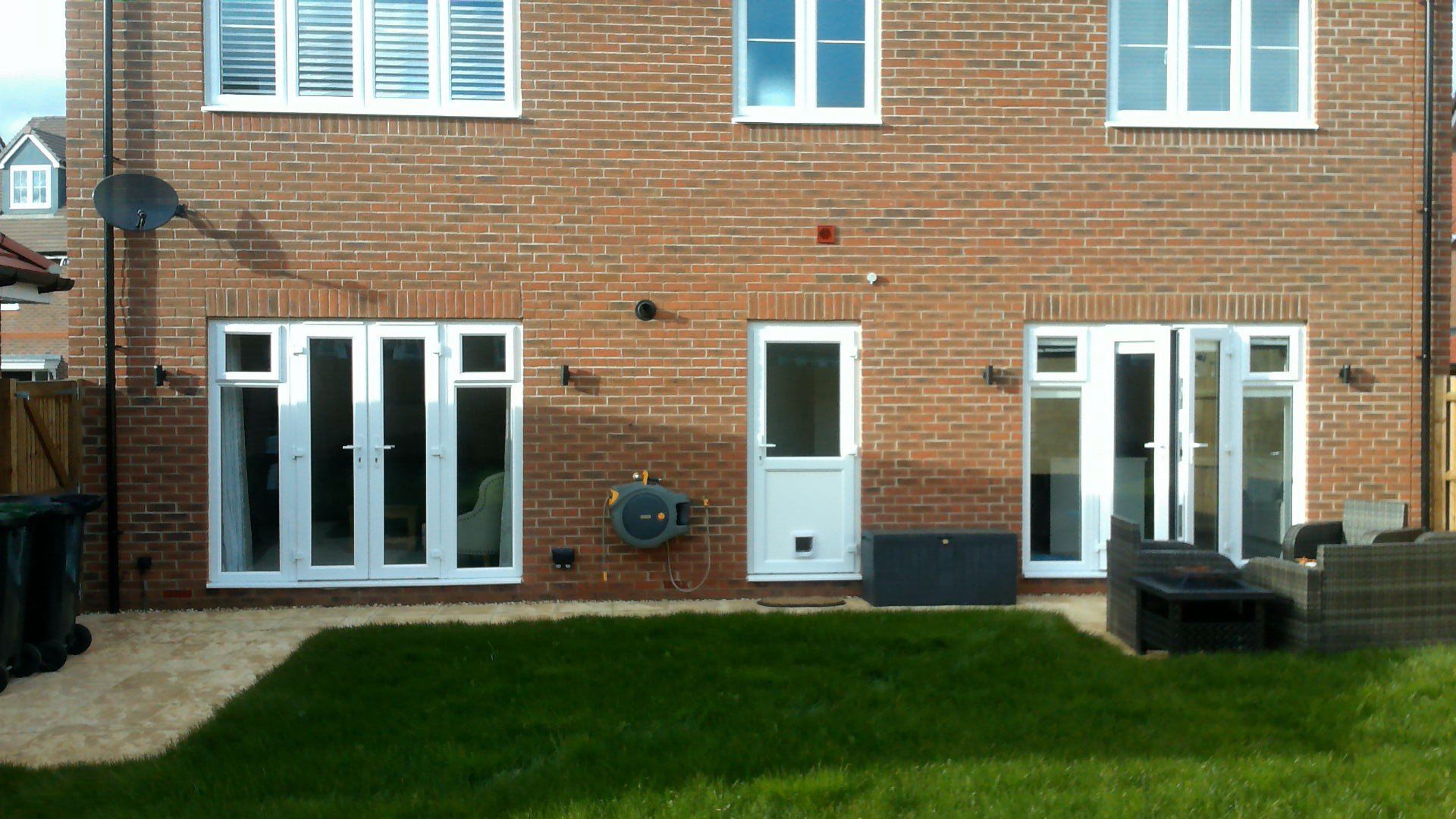 Back view of a brick house with white windows and doors, including two folding doors and a single door; a green lawn.