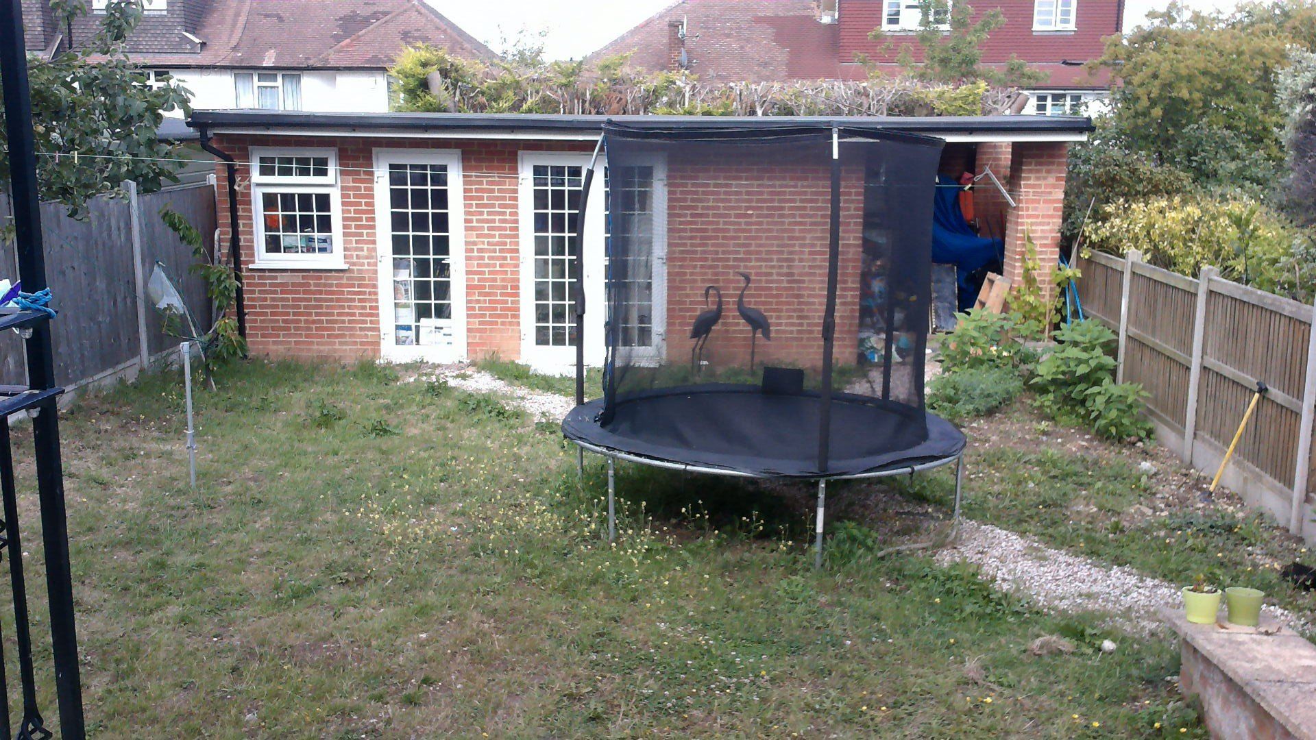 Backyard with a brick shed, trampoline, and patchy grass.