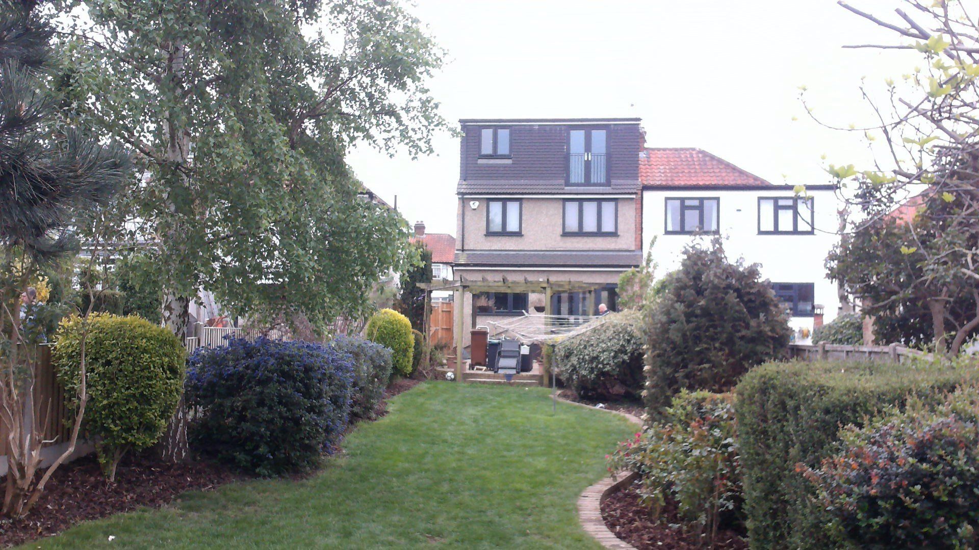 Backyard view with a lawn, garden beds, and a two-story house with a modern addition.