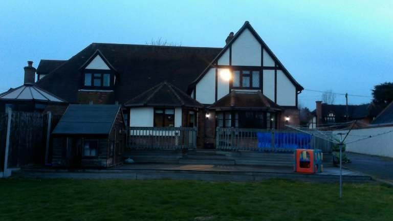Tudor-style building with white and brown exterior.  Grass lawn in front, steps up to the porch. Dusk setting.