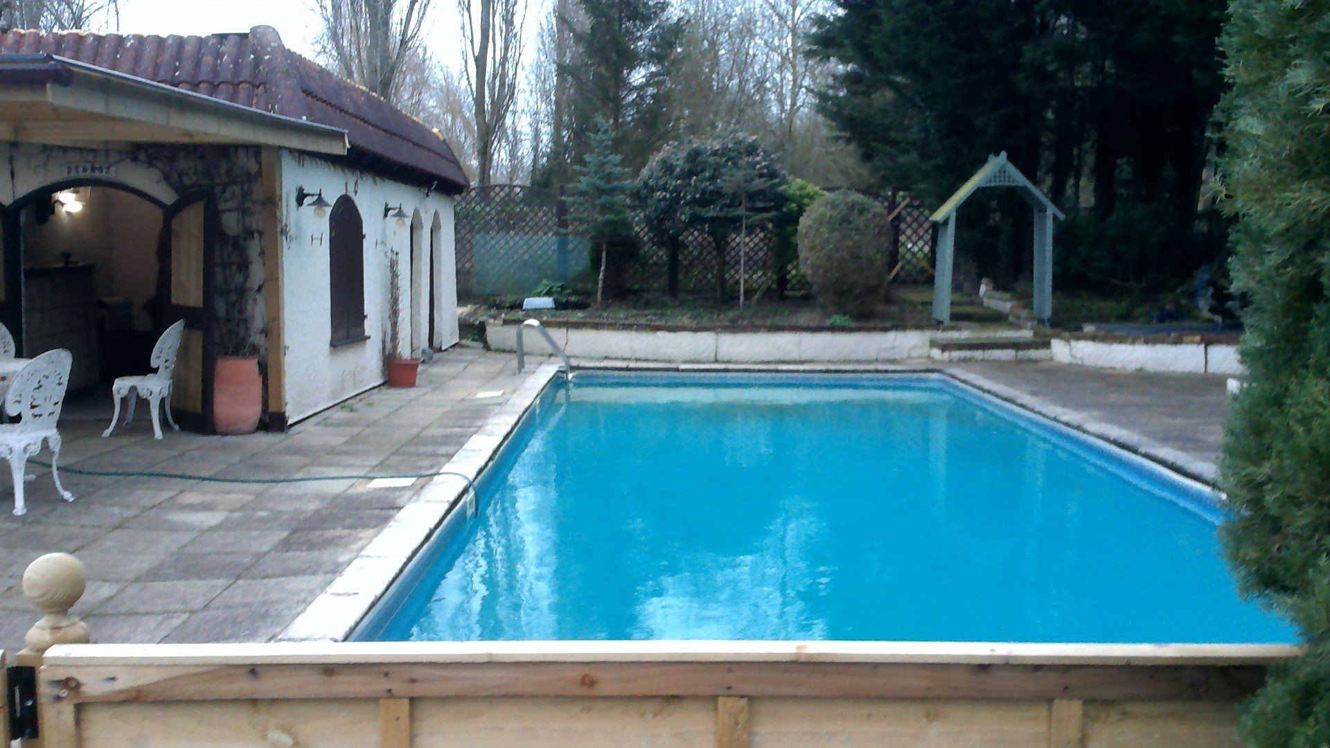 Swimming pool with blue water next to a building with arched doorways.