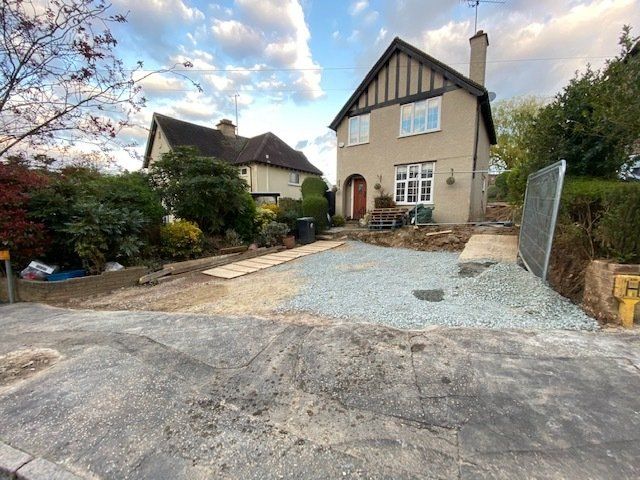 House with gravel driveway under construction; gray, blue, and beige colors; cloudy sky.