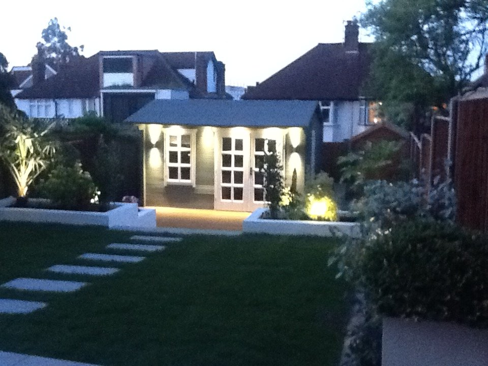 Backyard illuminated at dusk; shed with double doors, lit path, and landscaping.
