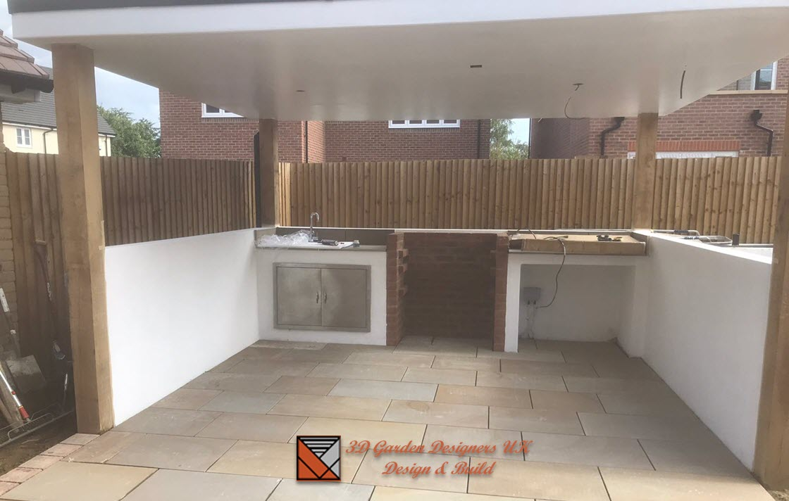 outdoor kitchen and pergola Outdoor kitchen under a white roof. Beige stone floor, white walls, wood posts, and a bamboo fence.