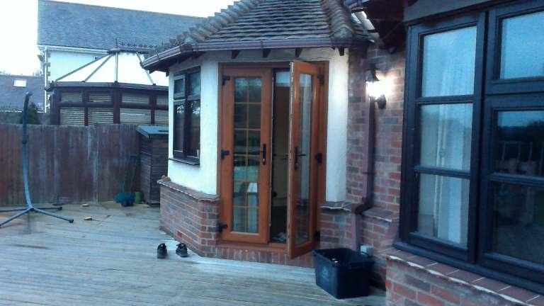 Exterior view of a house with brick and white walls, brown-framed doors and windows, and a tiled roof.