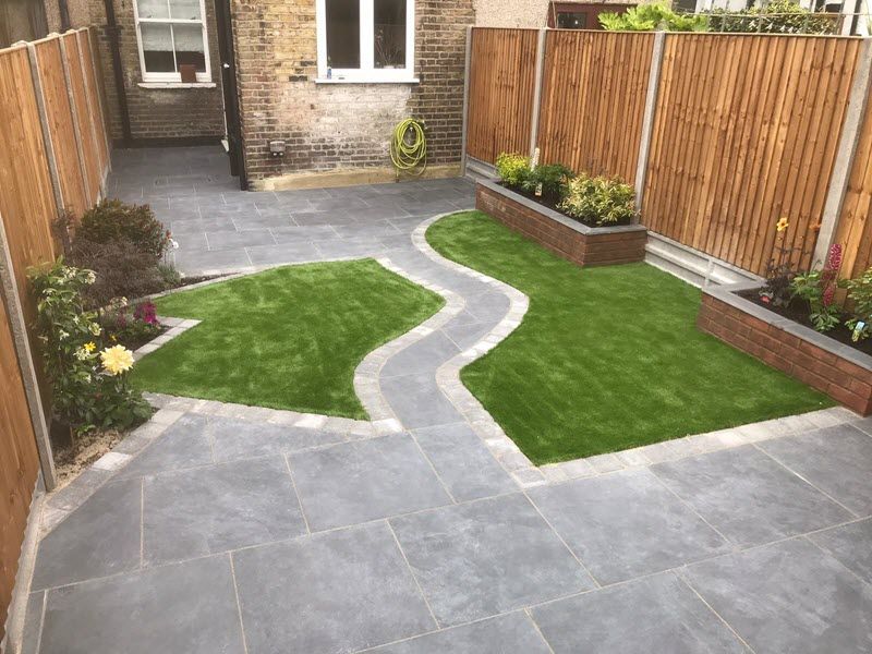 A backyard with gray paving, a winding path, green grass, and wooden fences.