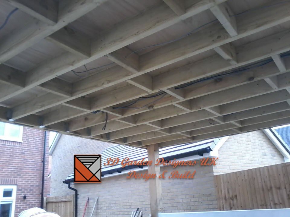 Underside view of a wooden deck frame, supported by posts, in a residential backyard.