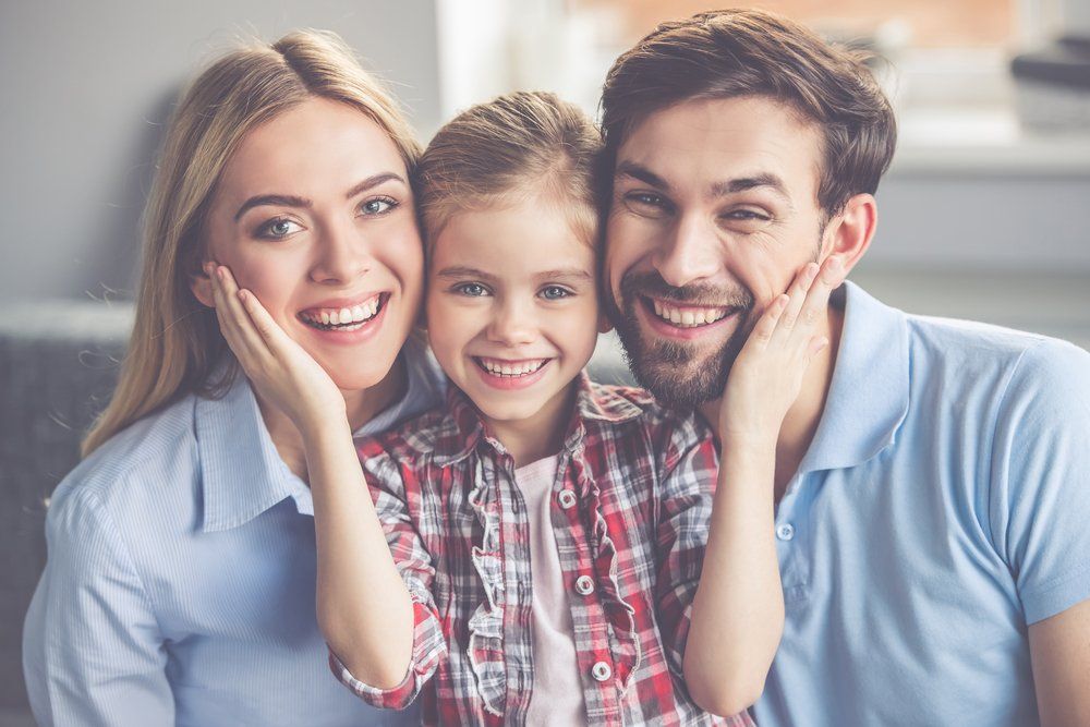 Smiling family of three posing closely together on a couch in a bright living room