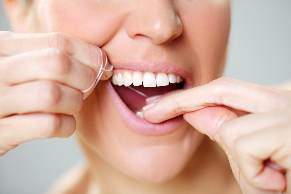 Hands flossing between white teeth in a close-up smile