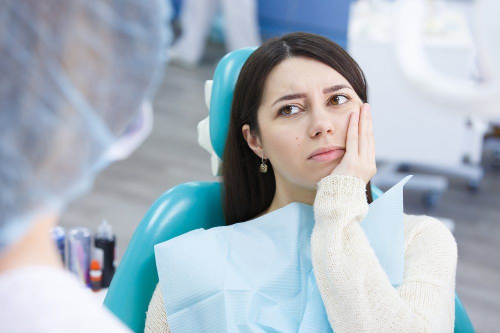 Woman holding her cheek in a dental chair, looking uncomfortable during a dental visit