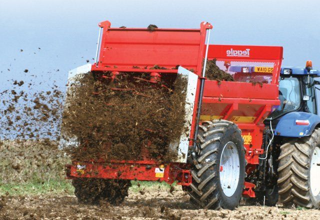Rød gødningsspreder på en traktor, der slynger jord ud over en mark