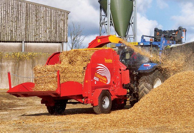 Rød høballepresser læsser halm ved siden af en traktor på en gårdsplads