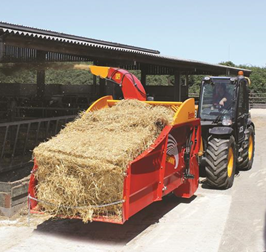 Traktor med halmpresser, der spreder halm på en gårdvej ved siden af en lade
