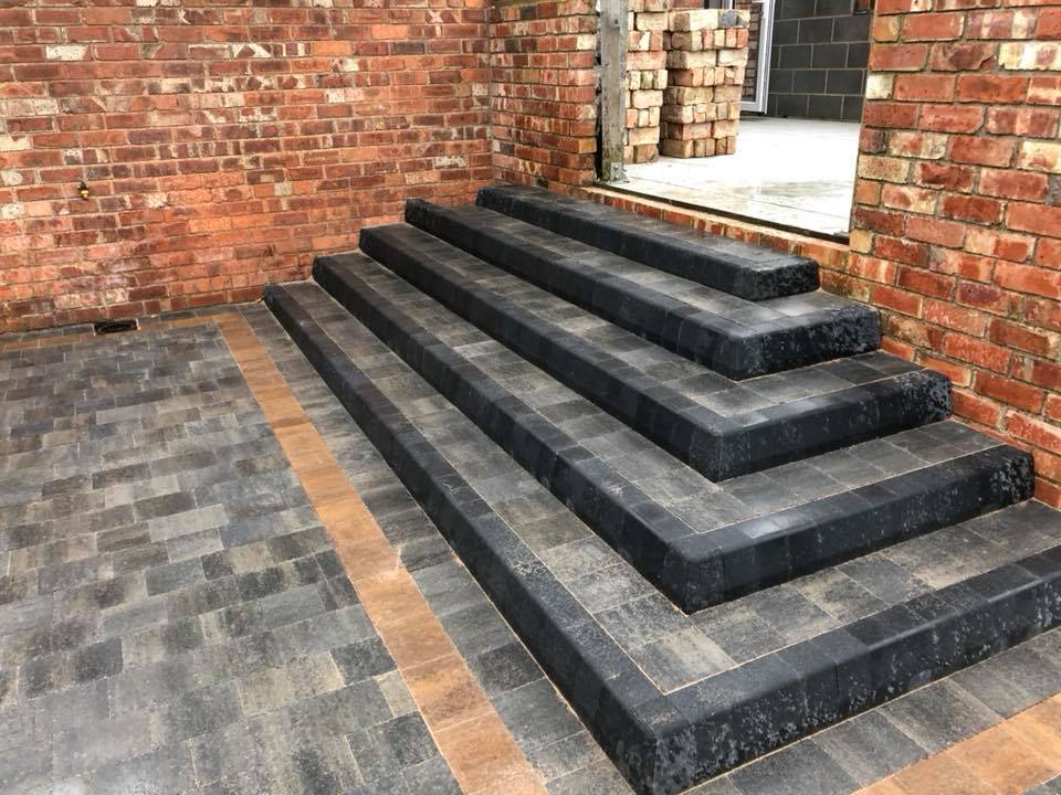 Brick stairs with dark stone steps leading to a doorway, beside a brick wall and paved patio