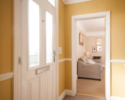 An interior view of a hallway with a front door entrance which leads to the lounge with sofa of a home.