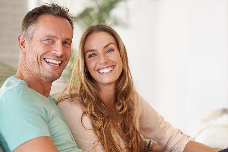 A man and a woman are sitting on a couch and smiling for the camera.
