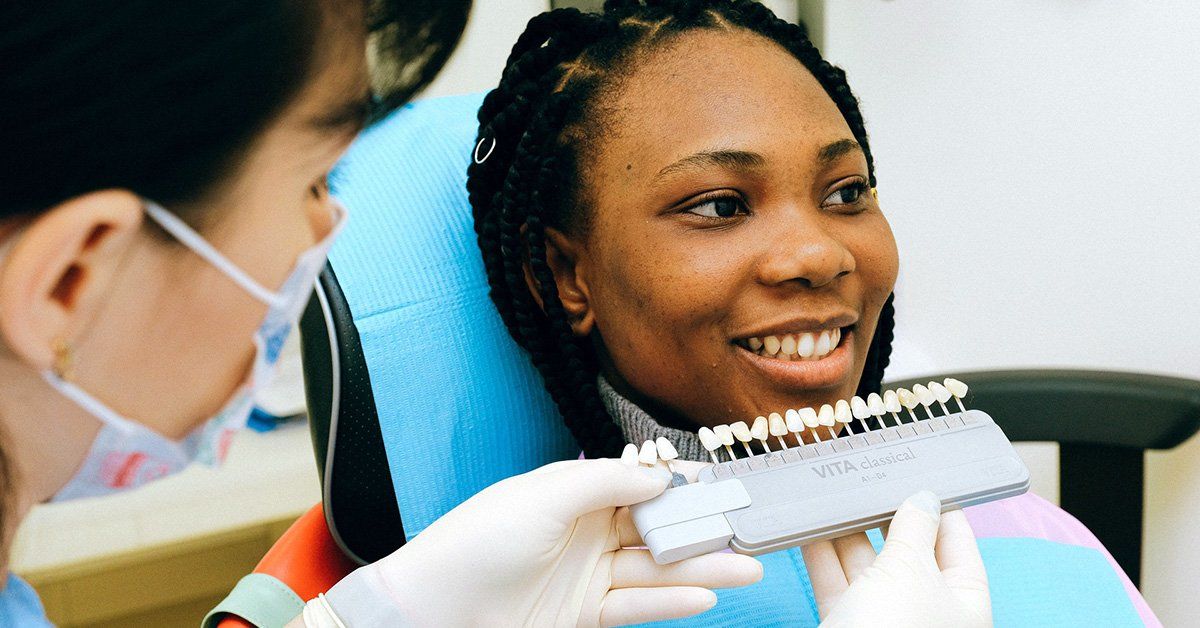A woman is sitting in a dental chair while a dentist examines her teeth.