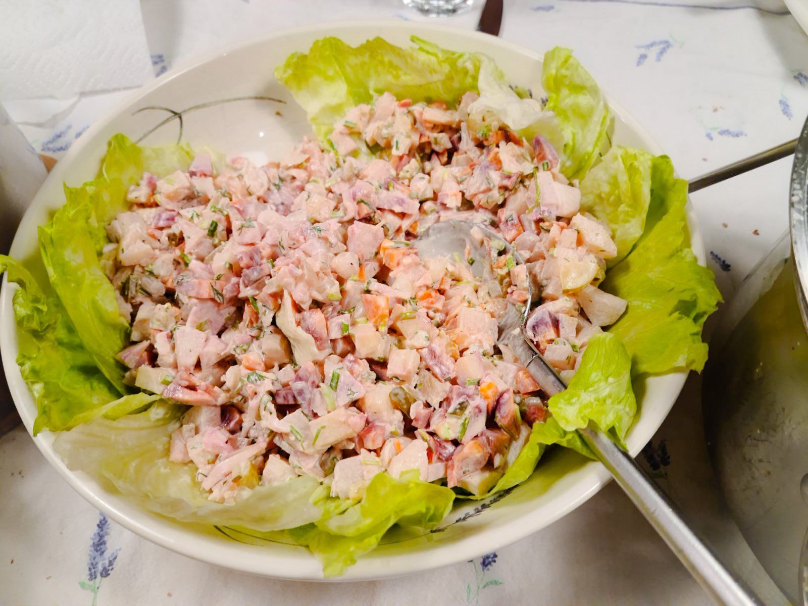 Een kom roze tonijnsalade op slabladeren met een lepel ernaast op het aanrecht.