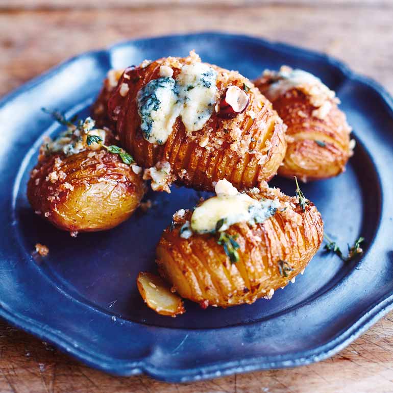 Geroosterde aardappelen met blauwe kaas en kruiden, geserveerd op een donkerblauw bord.