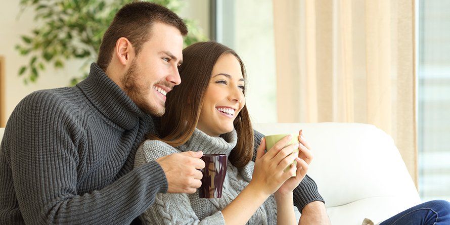 A couple sit on the couch together and drink coffee