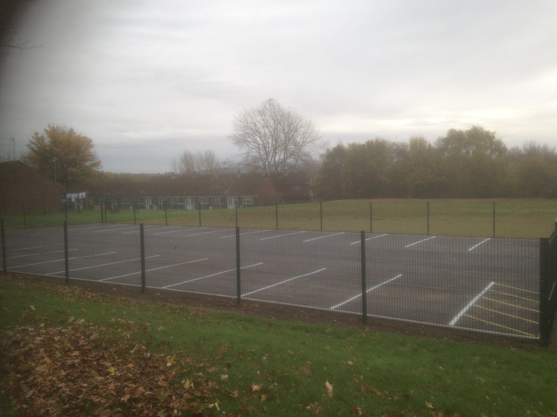 A fence surrounds a parking lot with trees in the background
