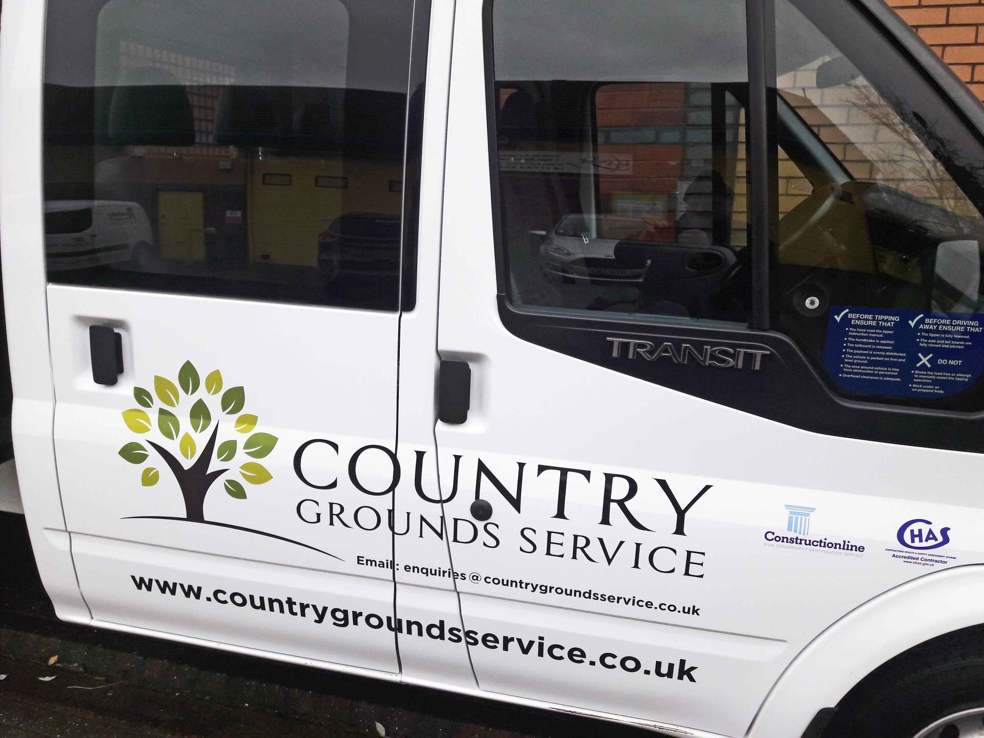 A white country grounds service van is parked in front of a brick building