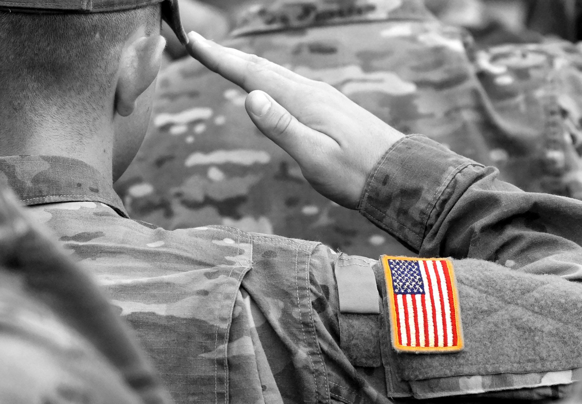 Soldier saluting, American flag patch on the sleeve; monochrome with colorized flag.
