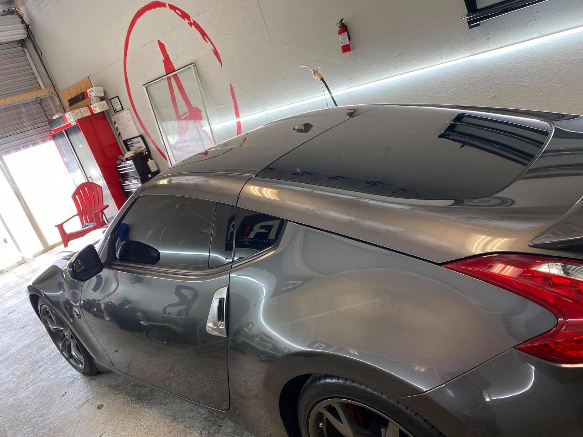 Gray sports car in a garage, with a dented rear side panel and red-marked damage area on the wall.