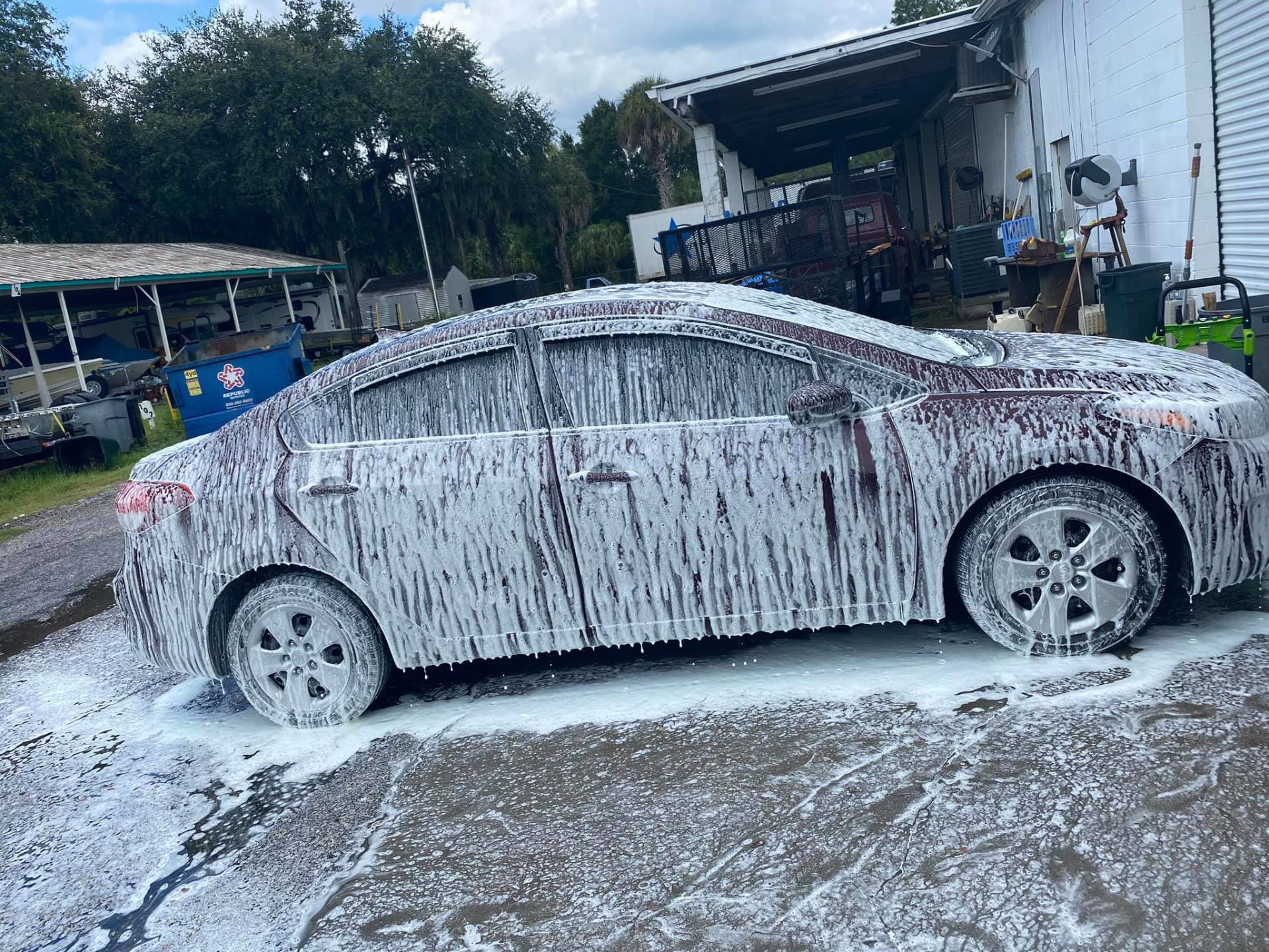 White car covered in thick foam at a car wash bay, with suds on the ground around it.