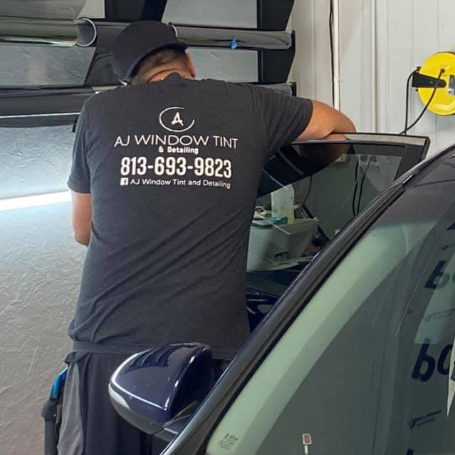 Technician in black shirt installing window tint beside a car in a garage