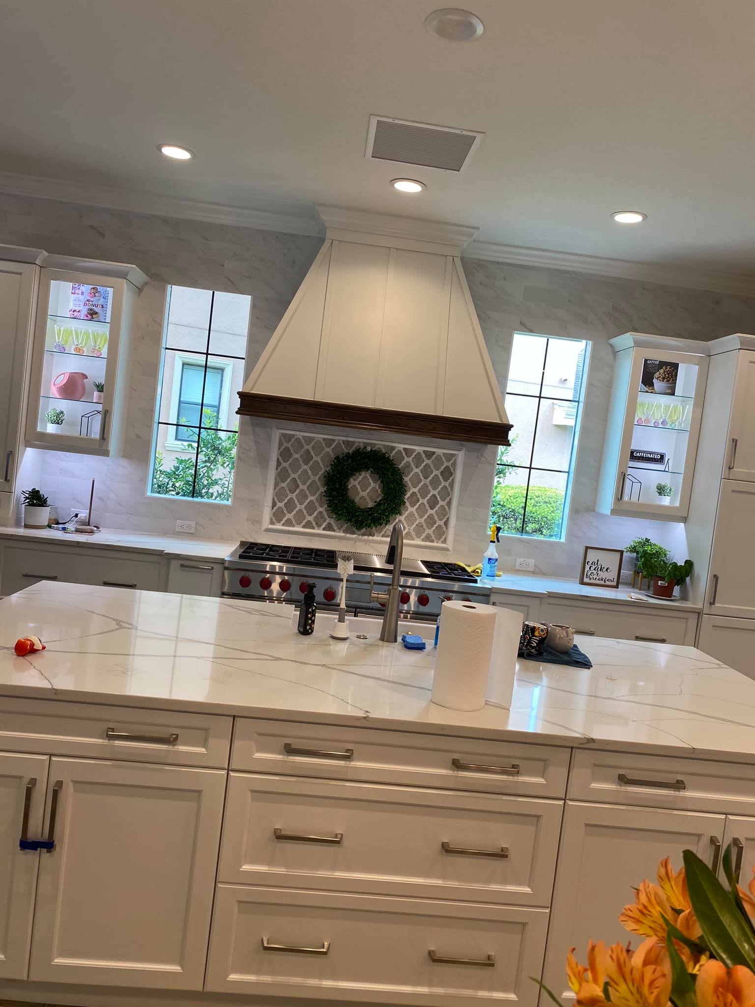 Bright white kitchen with island, pendant lights, and a large range hood centered on the back wall