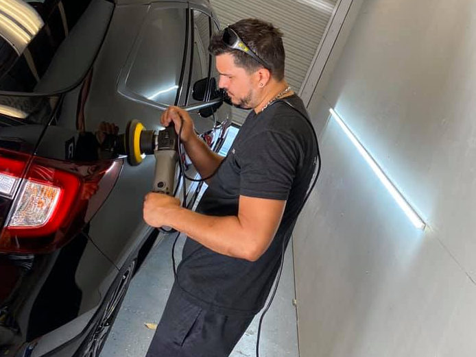 Man buffing a black car with a polishing machine in a garage-like space