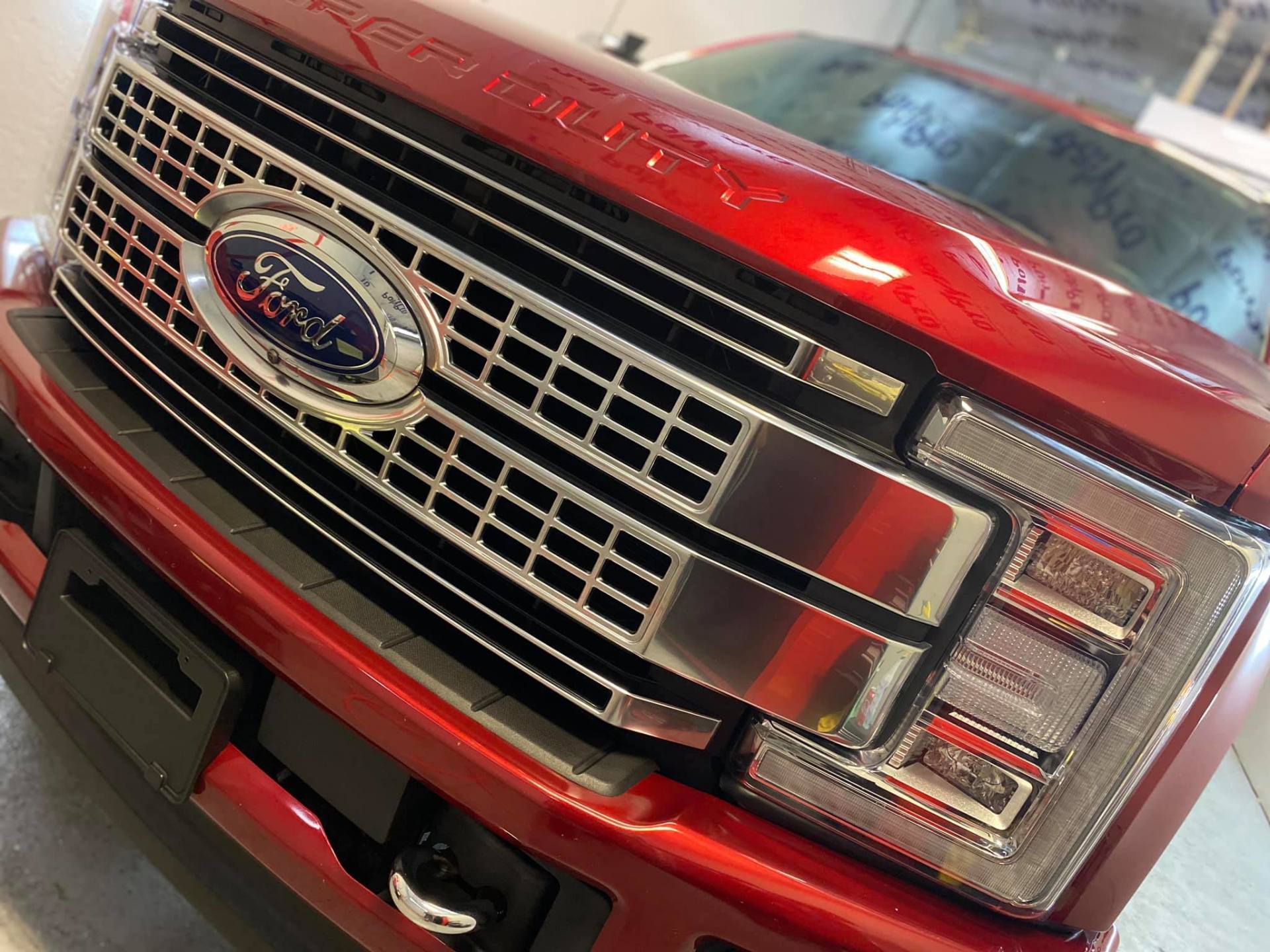 Close-up of a red Ford truck front grille and headlight on display indoors