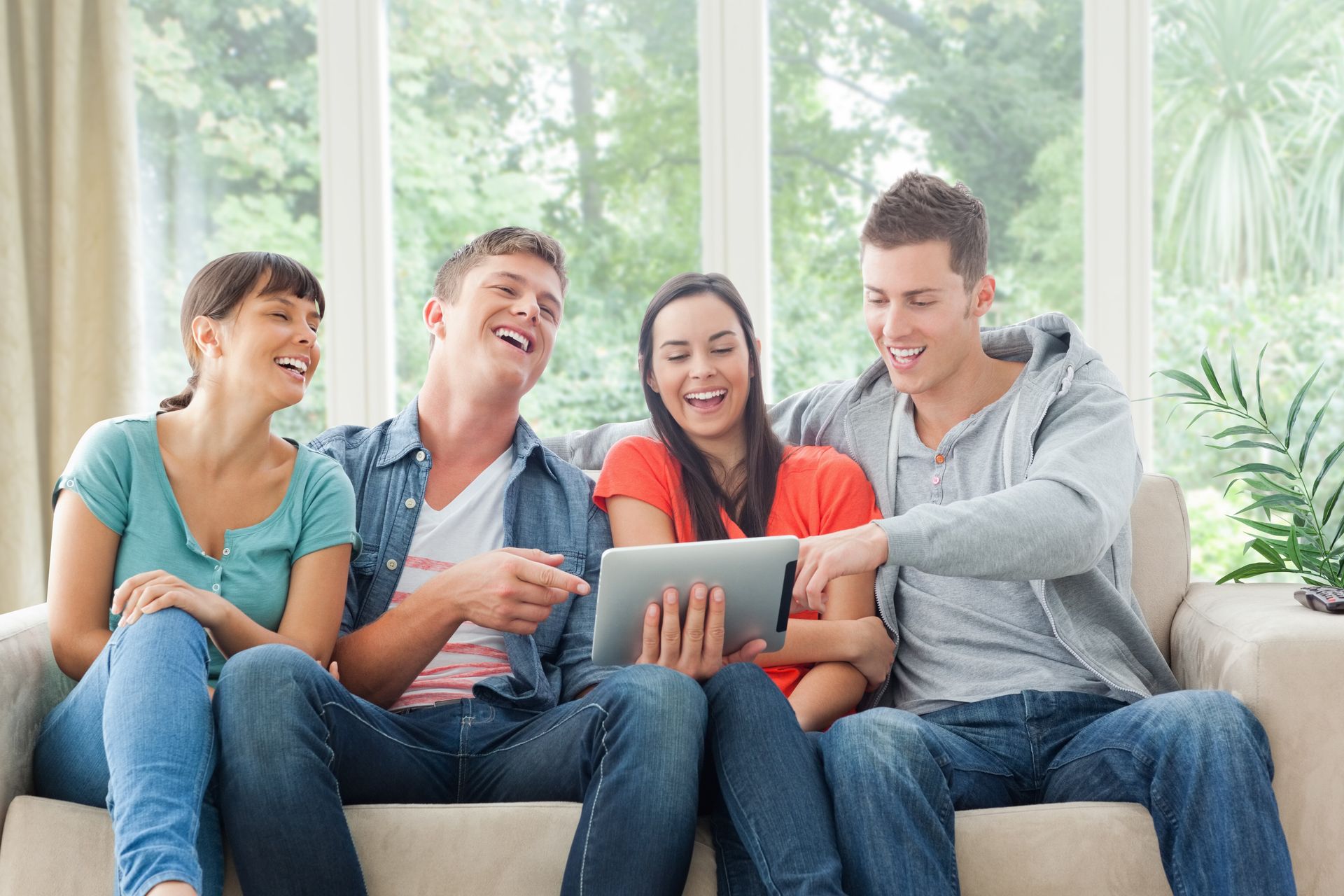 A group of people are sitting on a couch looking at a tablet.