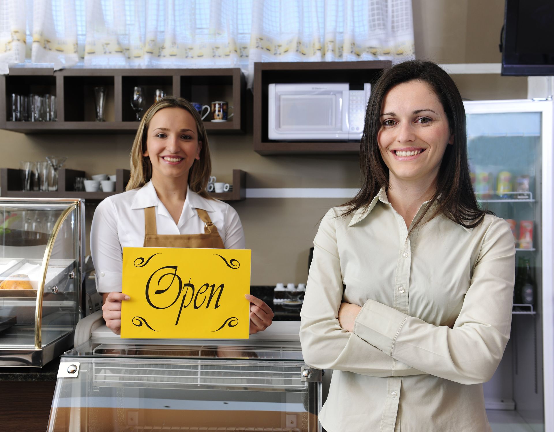Two women holding an open sign in a restaurant