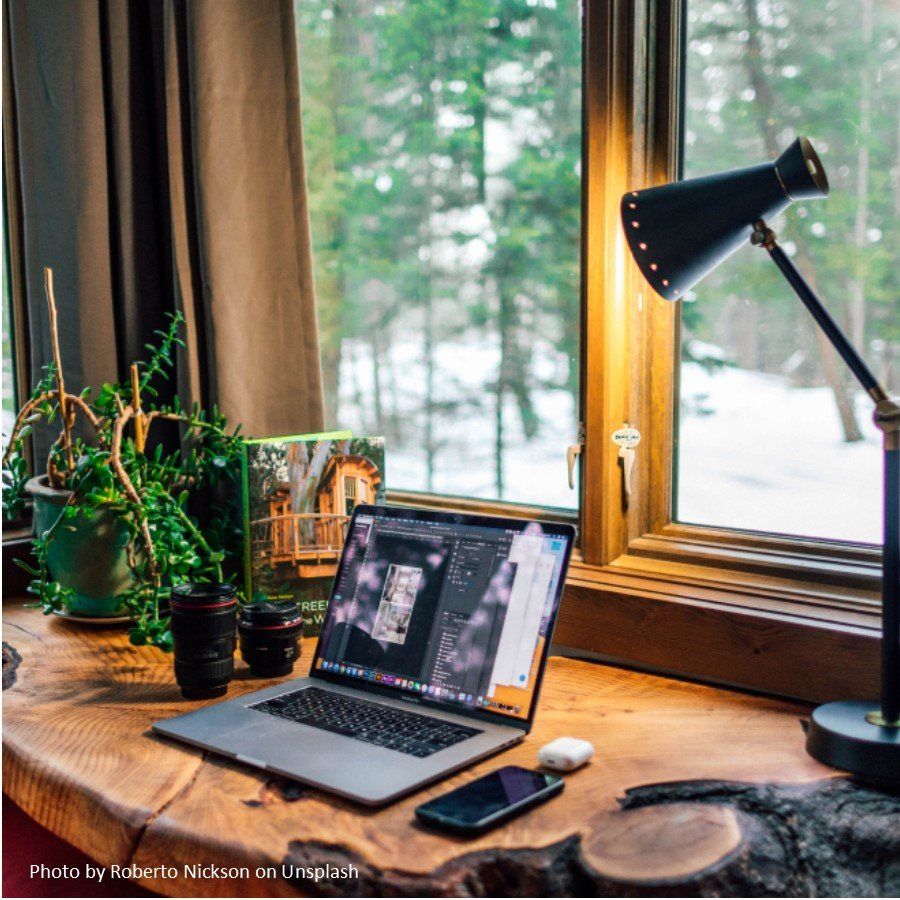 A laptop computer is sitting on a wooden desk in front of a window.