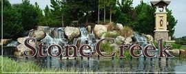 A stone creek sign with a waterfall in the background