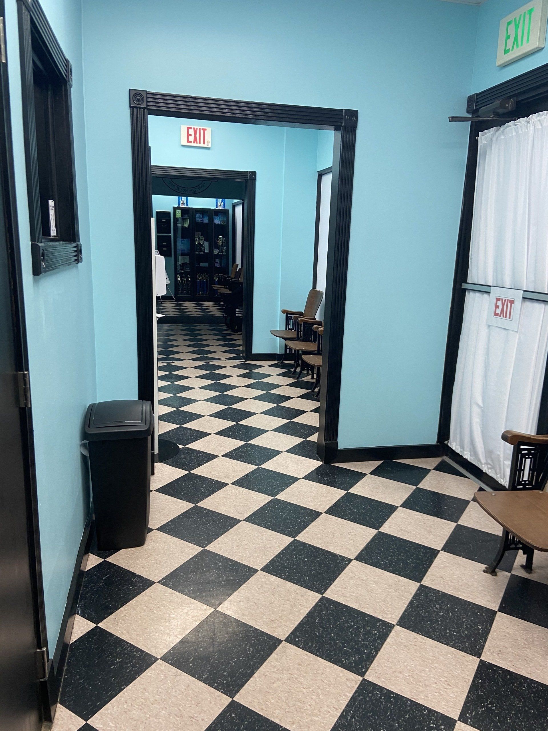 A hallway with a checkered floor and a trash can.