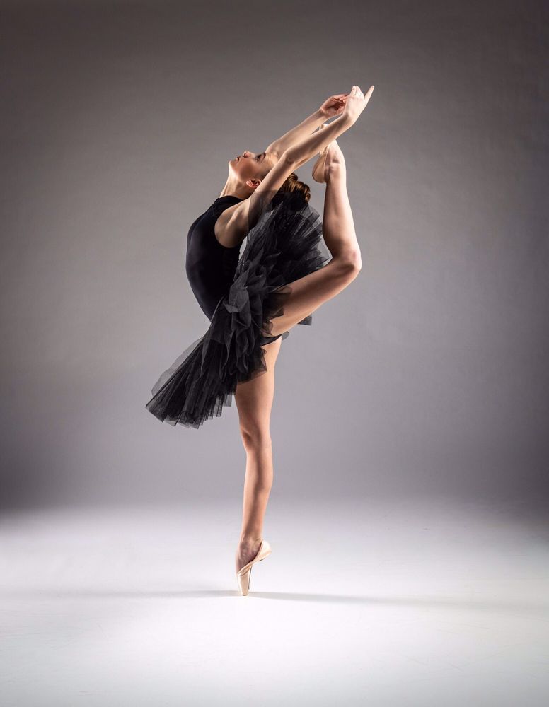 A ballerina in a black tutu is dancing on one leg.