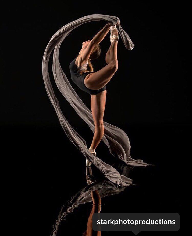 A woman in a black leotard is doing a split with a scarf.