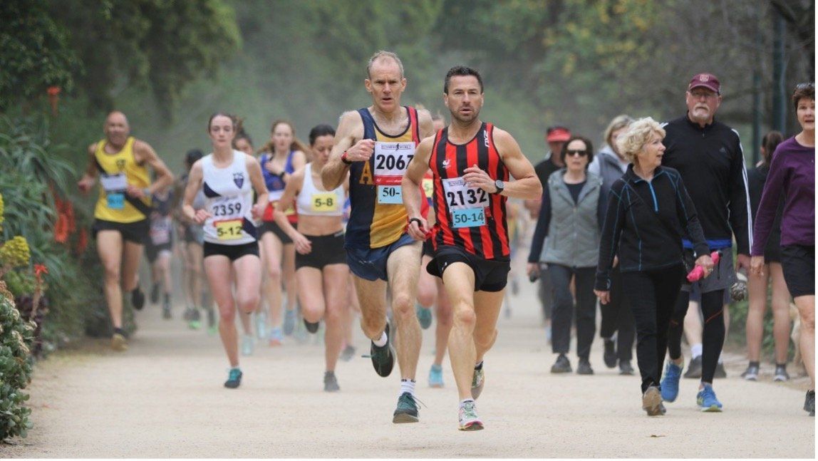 Darren running for mental health Darren the man behind run the tan is pictured running a race. Darren is at the front of the pack and wearing a black and red singlet with black shorts. He looks determined.
