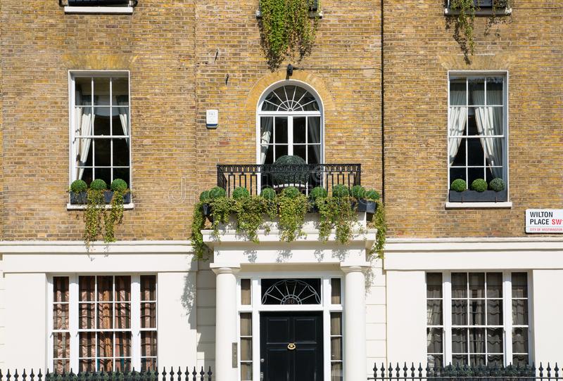 Brick building with white trim, arched doorway and balcony, black door, and potted plants.