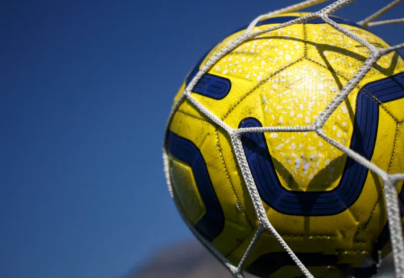 Yellow soccer ball in a white net against a blue sky.