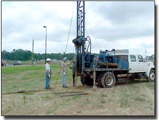 Geotechnical Engineering — Meridian, MS — Engineering Plus, Inc. Two men operating a drilling rig mounted on a truck in a field. Cloudy sky, roadside setting.